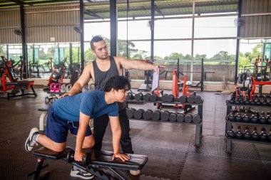 Erkek antrenör, spor salonundaki hizmetleri kullanmaya gelen müşterilere doğru egzersiz duruşlarını öğretiyor..