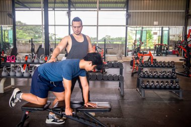 Erkek antrenör, spor salonundaki hizmetleri kullanmaya gelen müşterilere doğru egzersiz duruşlarını öğretiyor..