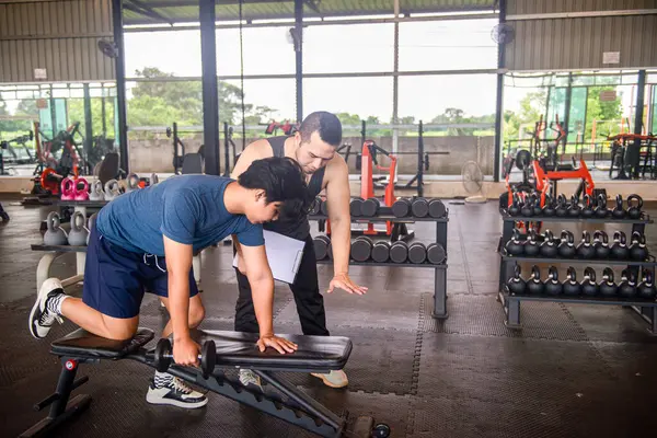 Erkek antrenör, spor salonundaki hizmetleri kullanmaya gelen müşterilere doğru egzersiz duruşlarını öğretiyor..