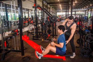 Erkek antrenör stajyerlere spor salonunda egzersiz malzemesi kullanmak için doğru duruşu öğretiyor.