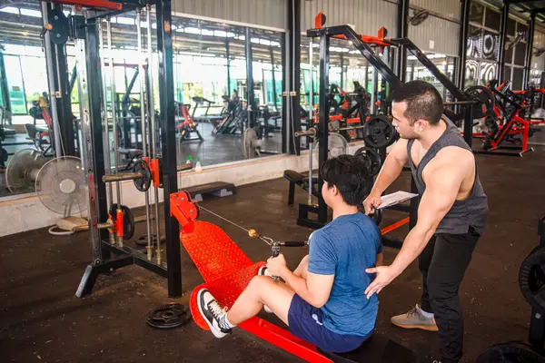 Erkek antrenör stajyerlere spor salonunda egzersiz malzemesi kullanmak için doğru duruşu öğretiyor.