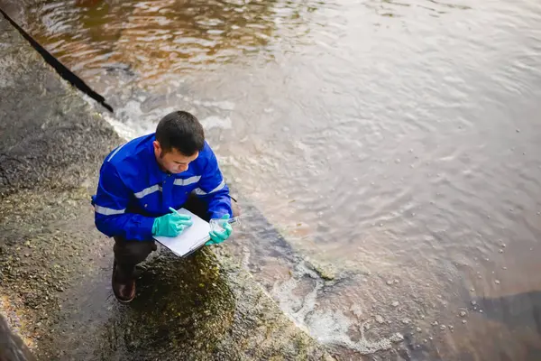 Bir su kaynağı mühendisi suyun saflığını bilimsel bir cam şişede kontrol eder ve kağıda kaydeder..