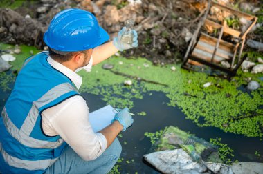 Su kaynakları uzmanları kanaldaki çöplerle kirlenmiş bir kanaldaki su kalitesini kontrol ediyorlar..