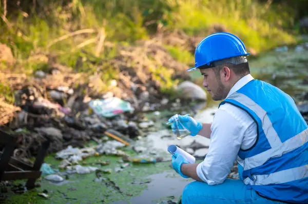 Su kaynakları uzmanları kanaldaki çöplerle kirlenmiş bir kanaldaki su kalitesini kontrol ediyorlar..
