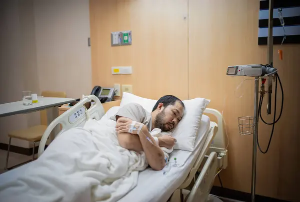 Bir erkek hasta hastane odasında yatıyor, tedavi görüyor, yorgun ve yalnız..