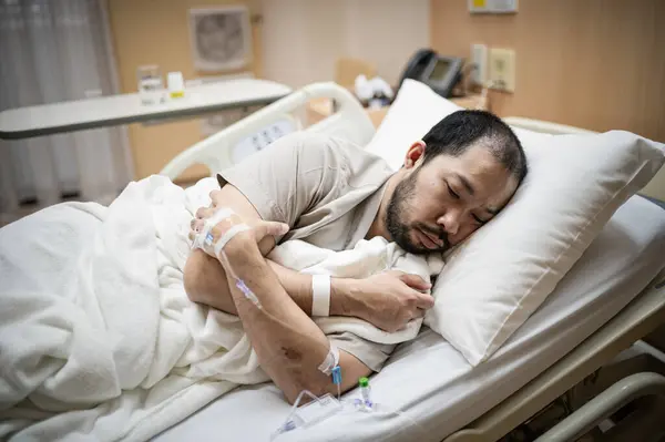 Bir erkek hasta hastane odasında yatıyor, tedavi görüyor, yorgun ve yalnız..