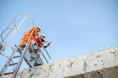 İki bakım teknisyeni ve güneş paneli yükleyicisi bir binanın çatısına güneş hücreleri yerleştirmeyi planlıyor..