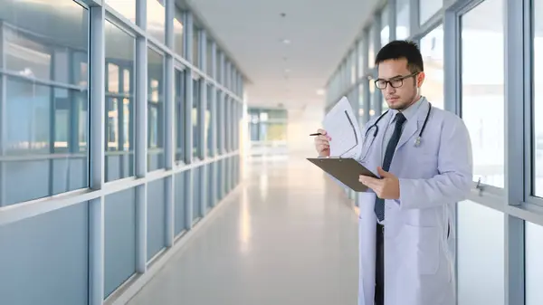 Doktor hastane koridorunda duruyor ve hastaların listesini kontrol ediyor..