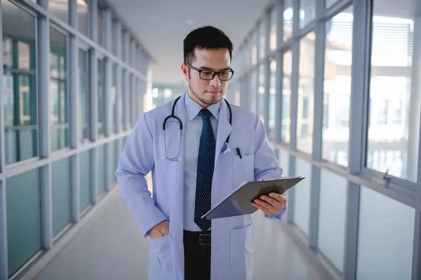 Bir erkek doktor hastane koridorundaki hastaların listesini kontrol ediyor..