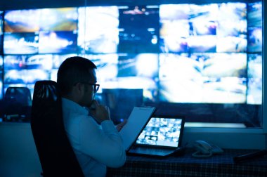 CCTV memuru panoda oturup raporları kontrol ediyor. birden fazla monitörün arka planına sahip