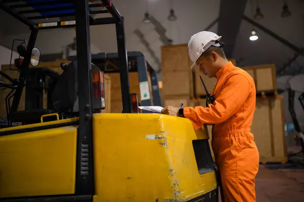Bir paket müfettişi bir depoda kutuları kontrol edip forkliftin arkasında notlar alıyor.