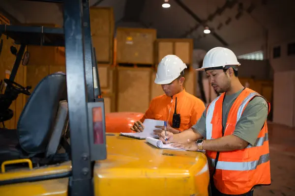 İki depo müfettişi kutulara bakmak ve not almak için bir forkliftin arkasında duruyorlar..