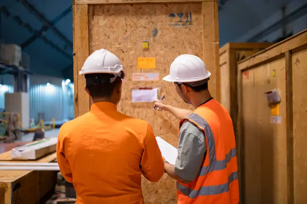 İki memur bir depoda büyük bir ahşap kolinin durumunu kontrol ediyor..