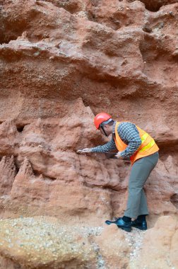 Bir jeolog mineralleri aramak için kayaların yakınındaki toprağı ve kayaları inceliyor.