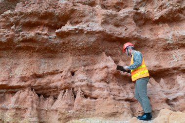 Bir jeolog mineralleri aramak için kayaların yakınındaki toprağı ve kayaları inceliyor.