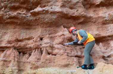 Bir jeolog mineralleri aramak için kayaların yakınındaki toprağı ve kayaları inceliyor.