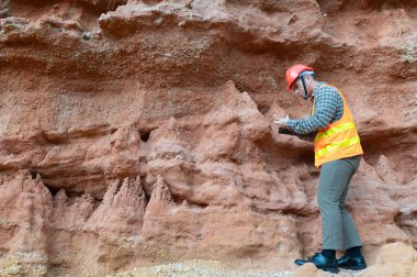 Bir jeolog mineralleri aramak için kayalıkların yakınındaki toprakları inceliyor.