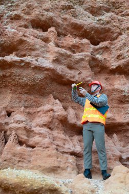 Bir jeolog uçurumun yakınındaki toprağa gömülen kayaların boyutlarını ölçmek için mezura kullanıyor.