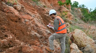 Jeolog, dağ alanındaki toprak ve kaya katmanlarının özelliklerini kaydediyor.