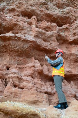 Bir jeolog uçurumun yakınındaki toprağa gömülen kayaların boyutlarını ölçmek için mezura kullanıyor.