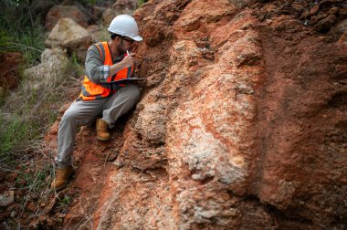 Bir jeolog, analiz için kaya örneği almak için bir kayayı delmek için çelik çubuk kullanıyor.