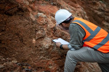 Bir jeolog, analiz için kaya örneği almak için bir kayayı delmek için çelik çubuk kullanıyor.