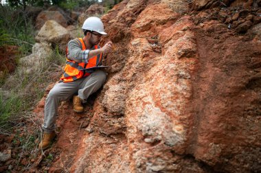 Bir jeolog, analiz için kaya örneği almak için bir kayayı delmek için çelik çubuk kullanıyor.