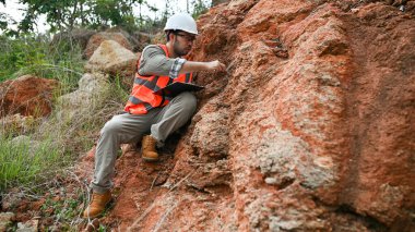 Bir jeolog, analiz için kaya örneği almak için bir kayayı delmek için çelik çubuk kullanıyor.