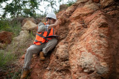 Bir jeolog, analiz için kaya örneği almak için bir kayayı delmek için çelik çubuk kullanıyor.
