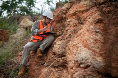 Bir jeolog, analiz için kaya örneği almak için bir kayayı delmek için çelik çubuk kullanıyor.