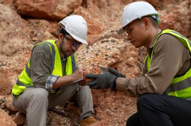 İki jeolog maden analizi için bir dağda toprak örnekleri topluyor.