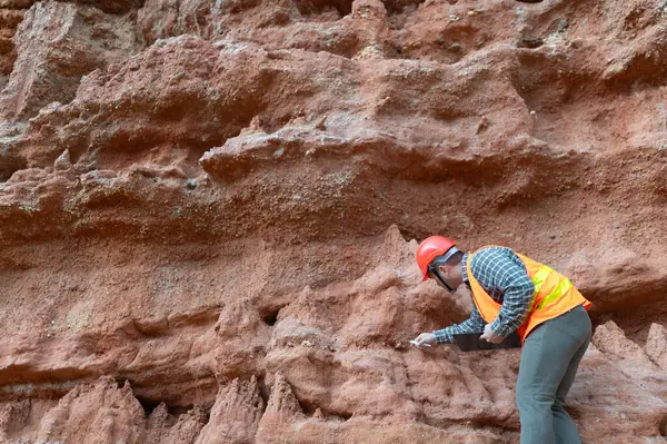 Bir jeolog mineralleri aramak için kayaların yakınındaki toprağı ve kayaları inceliyor.