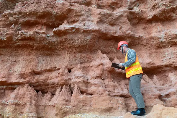 Bir jeolog mineralleri aramak için kayaların yakınındaki toprağı ve kayaları inceliyor.