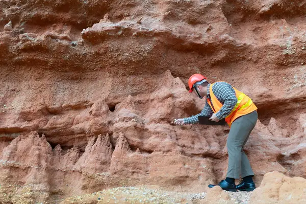 Bir jeolog mineralleri aramak için kayaların yakınındaki toprağı ve kayaları inceliyor.