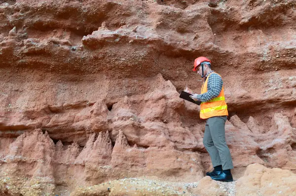 Bir jeolog mineralleri aramak için kayaların yakınındaki toprağı ve kayaları inceliyor.