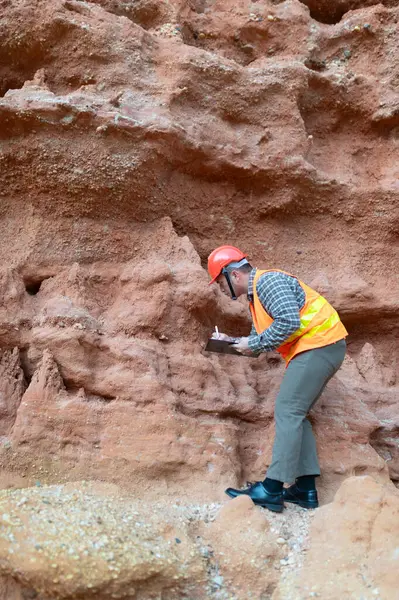 Bir jeolog mineralleri aramak için kayaların yakınındaki toprağı ve kayaları inceliyor.