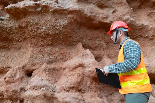 Bir jeolog mineralleri aramak için uçurumun kenarındaki katmana bakıyor.