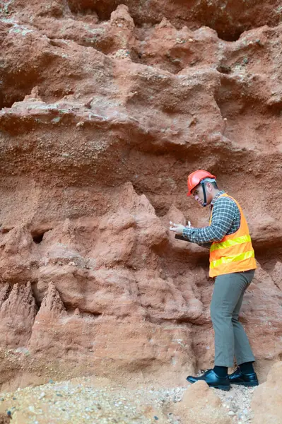 Bir jeolog mineralleri aramak için kayalıkların yakınındaki toprakları inceliyor.
