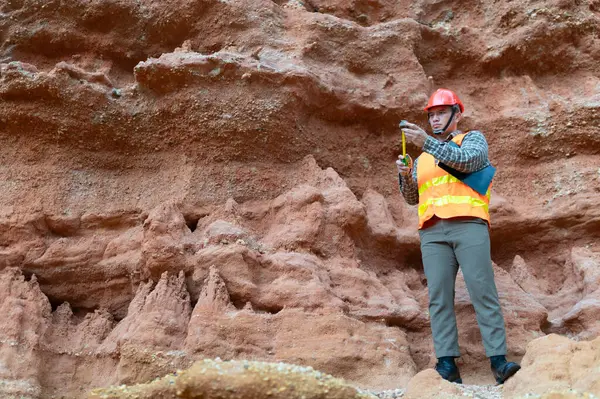 Bir jeolog uçurumun yakınındaki toprağa gömülen kayaların boyutlarını ölçmek için mezura kullanıyor.