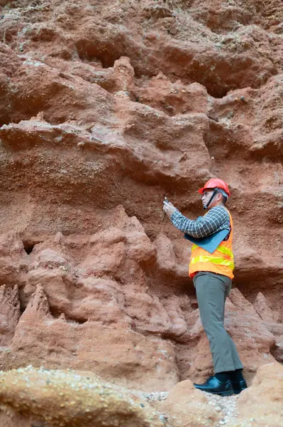 Bir jeolog uçurumun yakınındaki toprağa gömülen kayaların boyutlarını ölçmek için mezura kullanıyor.