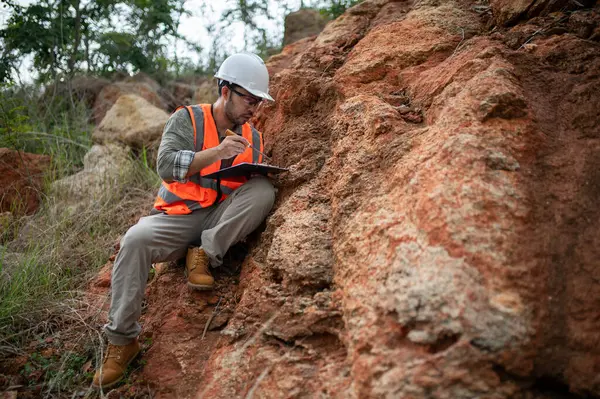 Bir jeolog, analiz için kaya örneği almak için bir kayayı delmek için çelik çubuk kullanıyor.