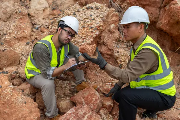 İki jeolog maden analizi için bir dağda toprak örnekleri topluyor.