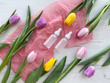 Lalelerle çevrili serum için beyaz kozmetik şişeler. Pembe kağıt üzerinde kozmetik ürünler