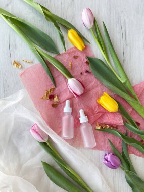 Lalelerle çevrili serum için beyaz kozmetik şişeler. Pembe kağıt üzerinde kozmetik ürünler