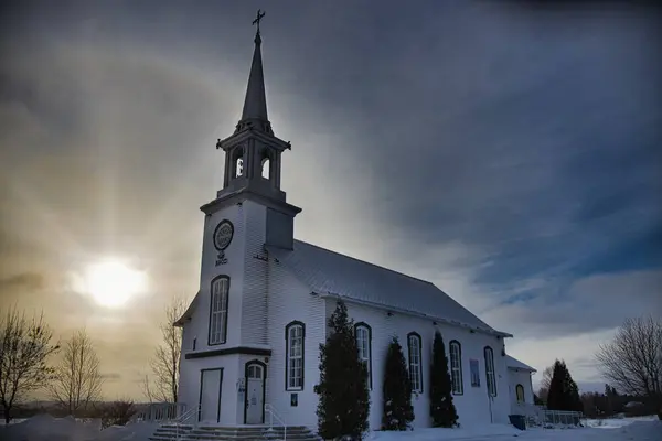 Kanada 'da küçük beyaz bir kilise. Mavi gökyüzü ve arkasında bulutlar var.