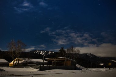 Gece yıldızlı gökyüzü ve köydeki dağlar.
