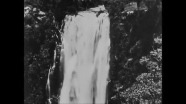 KENYA - 1930 - Kenya 'da bir safari grubu katırlarıyla nehri geçiyor ve manzaralı bir şelaleye hayran olmak için duruyor.