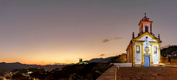 stock image Panoramic image with the baroque style churches and the city illuminated on top of the hill in Ouro Preto, Minas Gerais illuminated during dusk