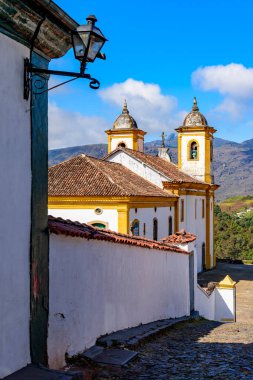 Minas Gerais 'deki Ouro Preto şehrinin arka planında dağlar olan eski renkli bir barok kilisesinin yan görüntüsü.