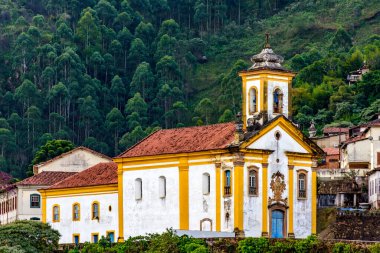 Minas Gerais 'in tarihi kenti Ouro Preto' daki ormanın önündeki barok kilisesi ve evler.